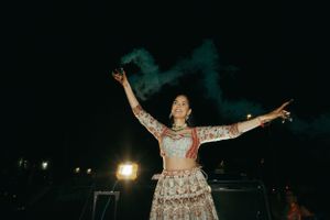 A performer dances with colored smoke against a dark night sky while wearing an embellished lehenga outfit.
