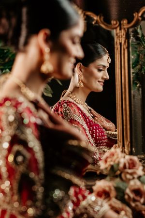 A reflection of traditional Indian bridal jewelry and attire with ornate red lehenga and statement earrings in an elegant setting.