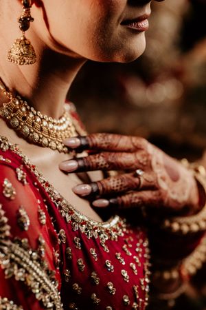Close-up of traditional Indian bridal jewelry and red lehenga with intricate henna designs on hands.