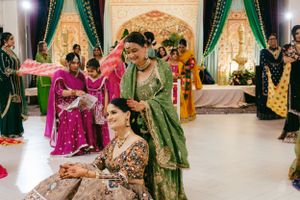 Traditional mehndi ceremony celebration with attendees in colorful saris and embroidered outfits at decorated indoor venue.