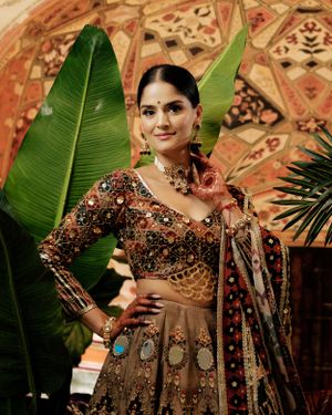 Elegant brown lehenga with detailed embellishments styled with tropical leaves and ornate mosaic backdrop.