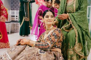 A person wearing traditional Indian bridal attire with henna decorated hands sits during a wedding celebration ceremony.