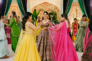 Wedding guests in vibrant yellow, pink and green lehengas dance together during festive Indian celebration.