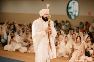 A group gathered for a Sikh wedding ceremony in white attire at an indoor venue.