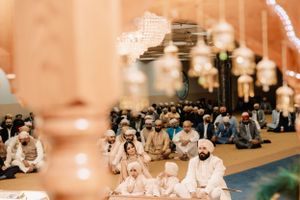 Muslim worshippers gather inside a mosque for prayer during Ramadan with blurred lantern lights in the foreground.