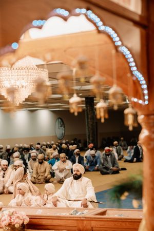 People gather for prayer inside a mosque with ornate chandeliers and decorative elements visible in the frame.