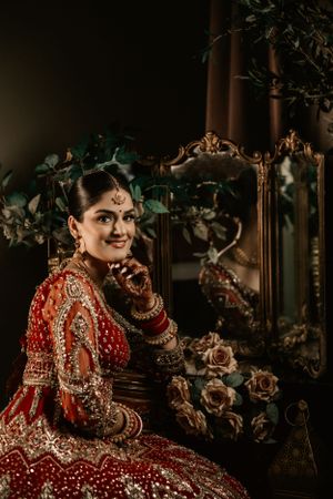 Traditional Indian bridal attire featuring an ornate red lehenga with intricate embroidery and jewelry in a vintage setting.