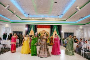 A festive wedding celebration with colorful traditional dresses in green, yellow, and pink on a bright dance floor.