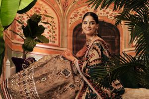 Traditional bridal attire with intricate embroidery and details is showcased against an ornate coral-colored architectural backdrop.