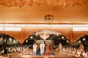 Under a peach-colored tent, people in white gather around a dance floor at an outdoor wedding reception.
