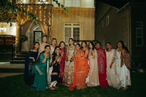 Group photo of wedding guests in colorful traditional Indian saris and formal wear at an evening celebration.