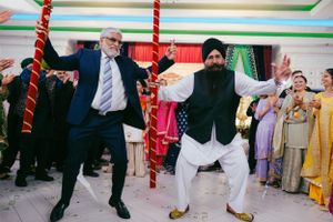 Two people dance energetically together at a colorful Indian wedding celebration with festive decorations in the background.