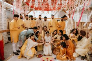 Traditional Indian wedding ceremony with guests wearing yellow and cream outfits during a ritual under pink floral decorations.
