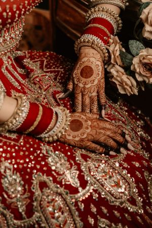 Intricate henna designs and jewelry on hands draped in luxurious red and gold traditional Indian bridal attire.