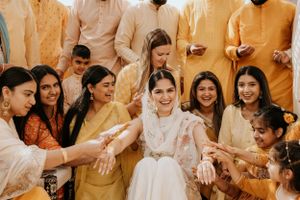 A joyous wedding celebration shows guests in traditional Indian attire gathered around a bride in white.
