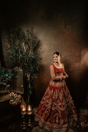 A stunning red and gold traditional bridal lehenga displayed in a moody setting with lanterns and greenery.