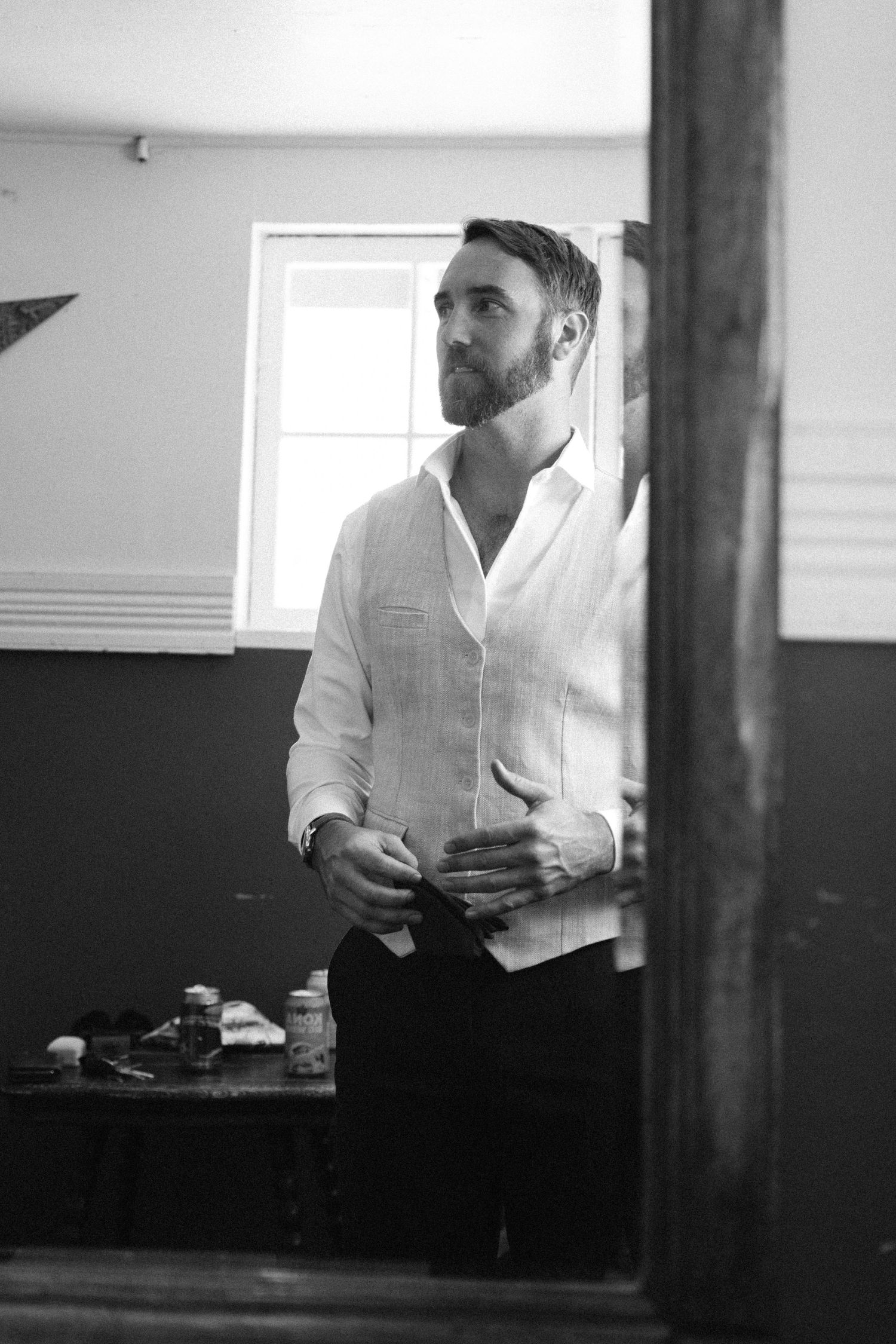 A person in a white shirt stands thoughtfully near a window in a black and white photograph.