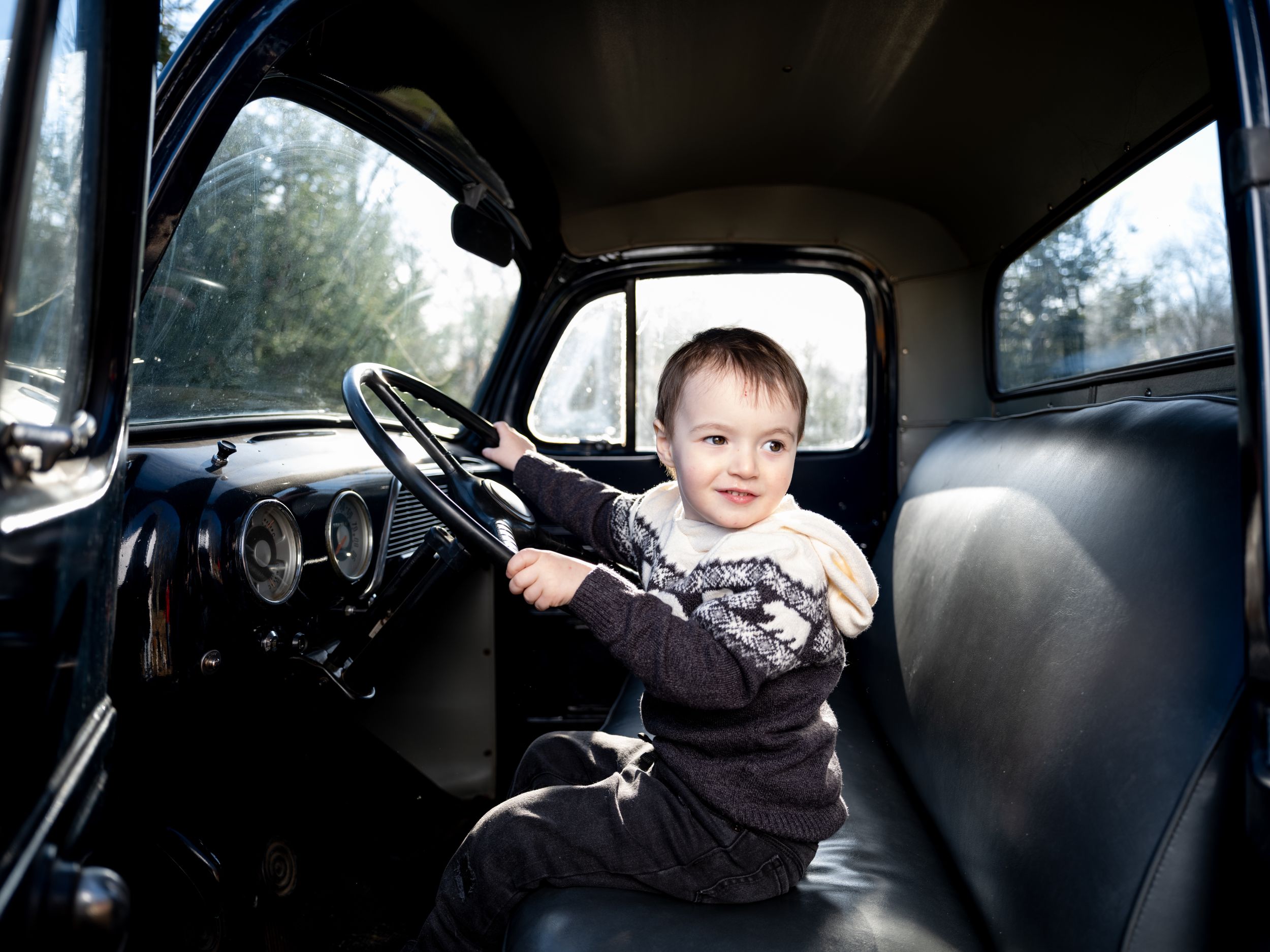 A vintage truck interior with dark leather seats and classic steering wheel photographed from the passenger side.