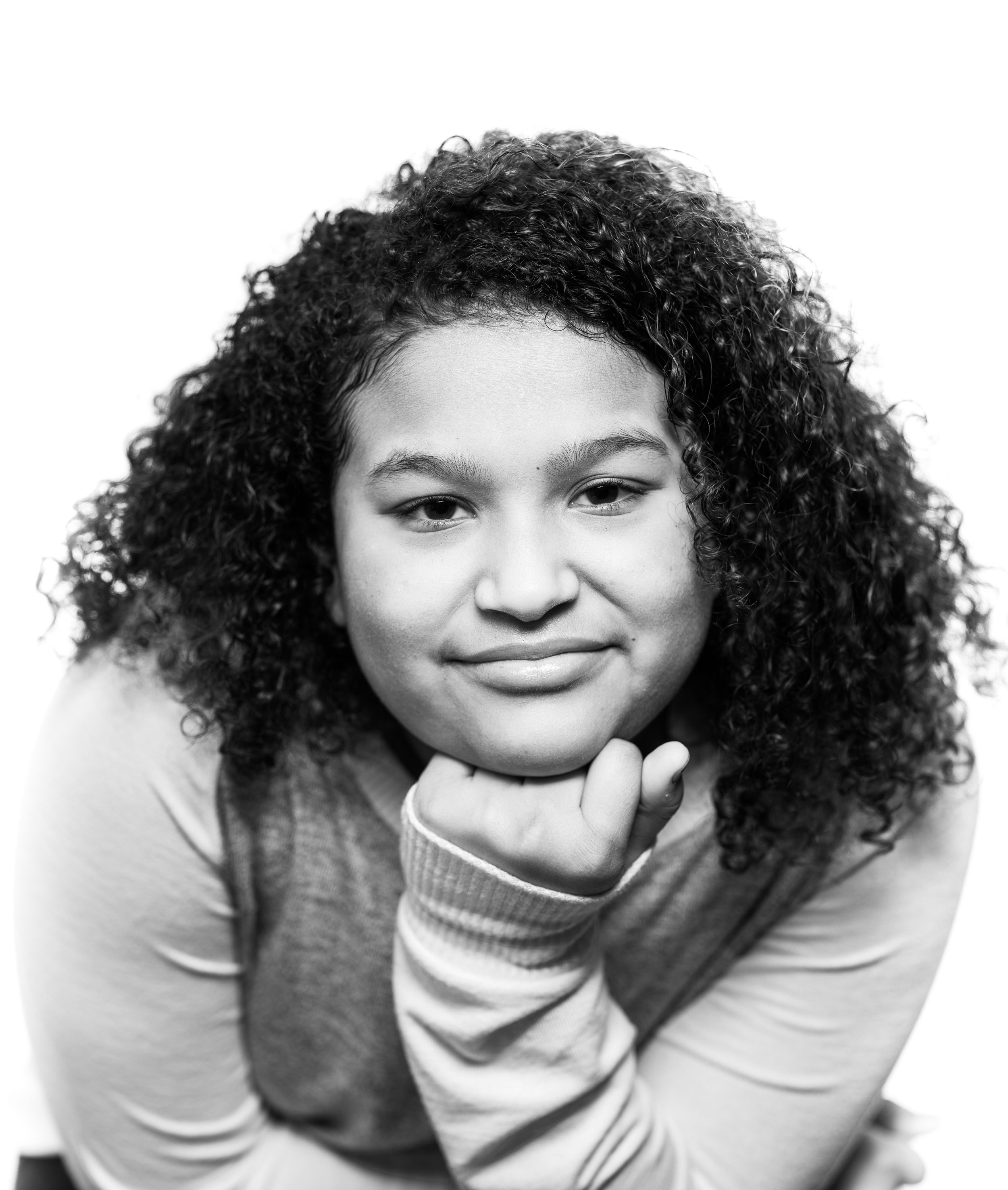 Black and white portrait of a person with curly natural hair smiling warmly while resting chin on hand.