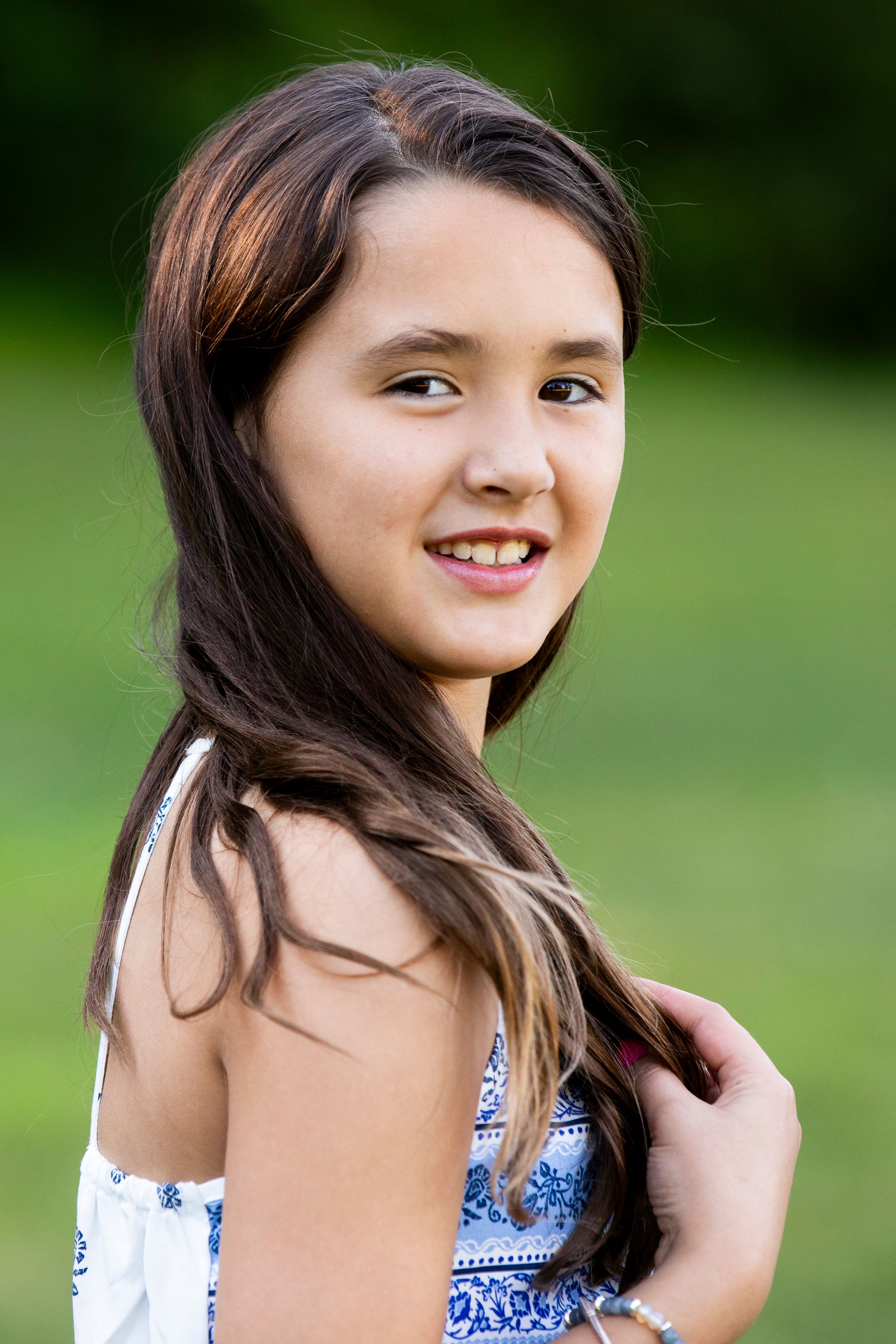 Portrait of a young person in a blue and white patterned sundress smiling against a blurred green outdoor background.