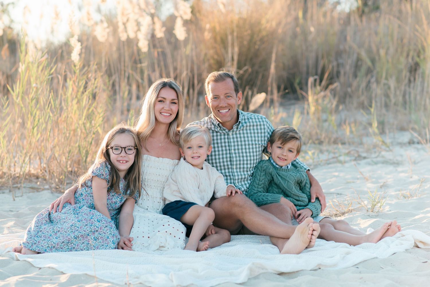 Family of five cuddled together on a blanket at Manasquan Beach, New Jersey, with fall grasses and overcast skies creating a soft, moody atm