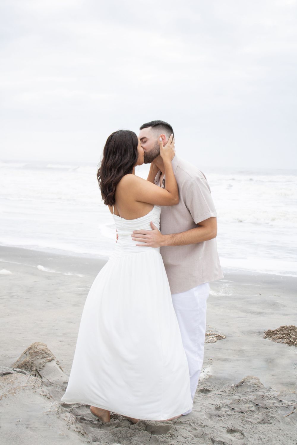 Romantic couple sharing an intimate kiss on a misty beach with waves crashing in the background.