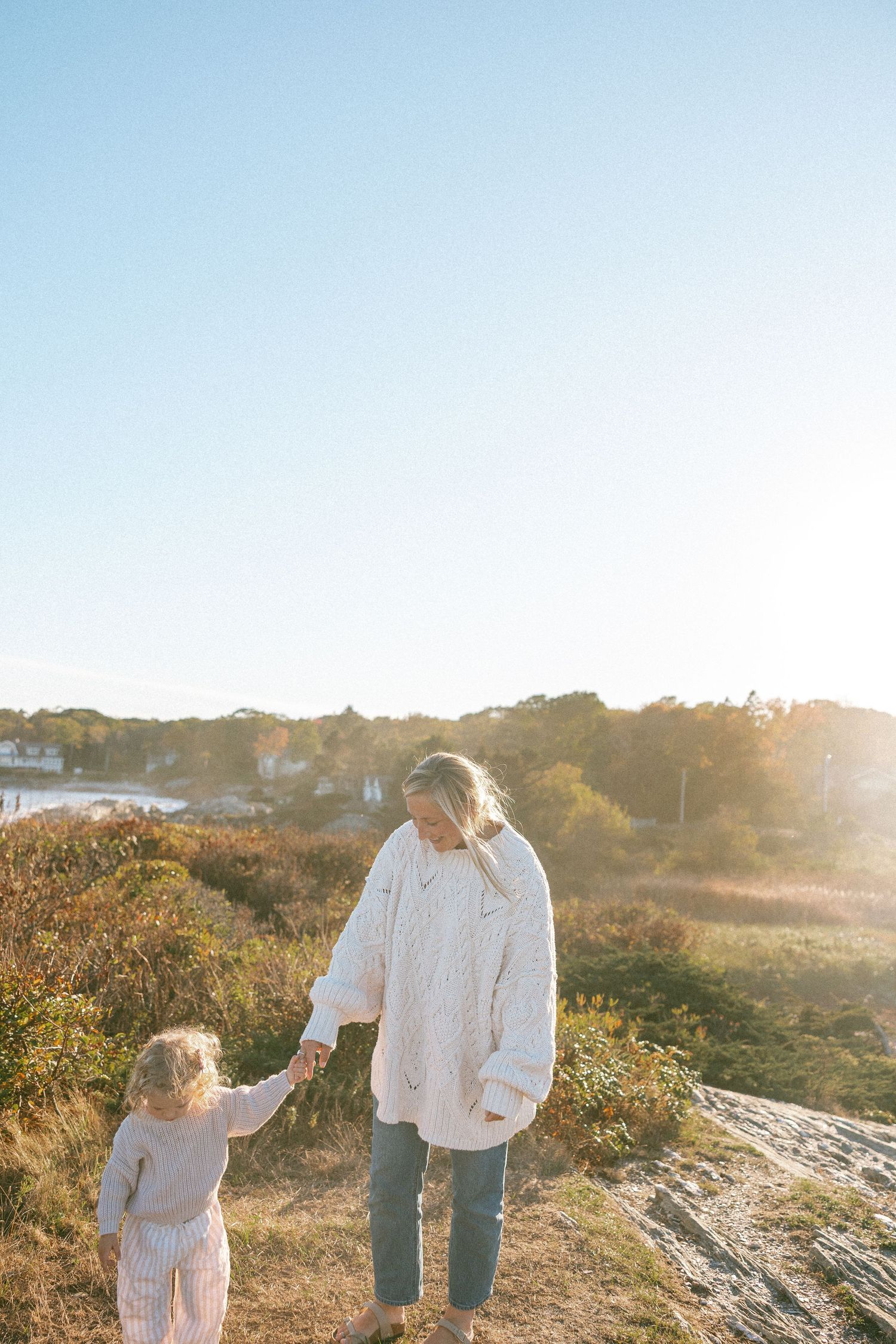 Two figures walk together along a scenic coastal path at sunset with golden light illuminating the landscape.
