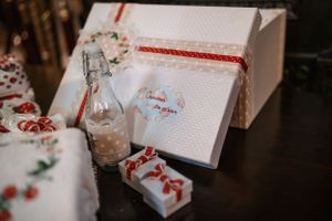 White gift box with red ribbon and decorative baptism accessories on dark surface.