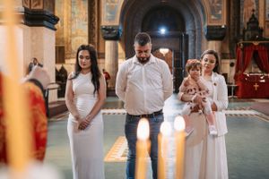 Family standing before lit candles during Orthodox baptism ceremony in church.