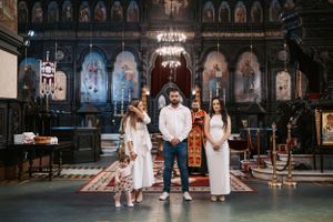 White-clad attendees gather in an ornate Orthodox church with decorated walls and chandeliers.