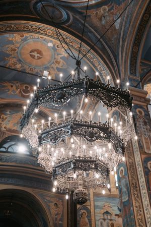 Crystal chandeliers hang from an intricately painted ceiling in an Orthodox church.