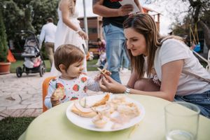 Small child eating at yellow outdoor table during a party.