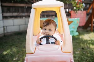Small toy car with pale yellow and pink colors in backyard setting.