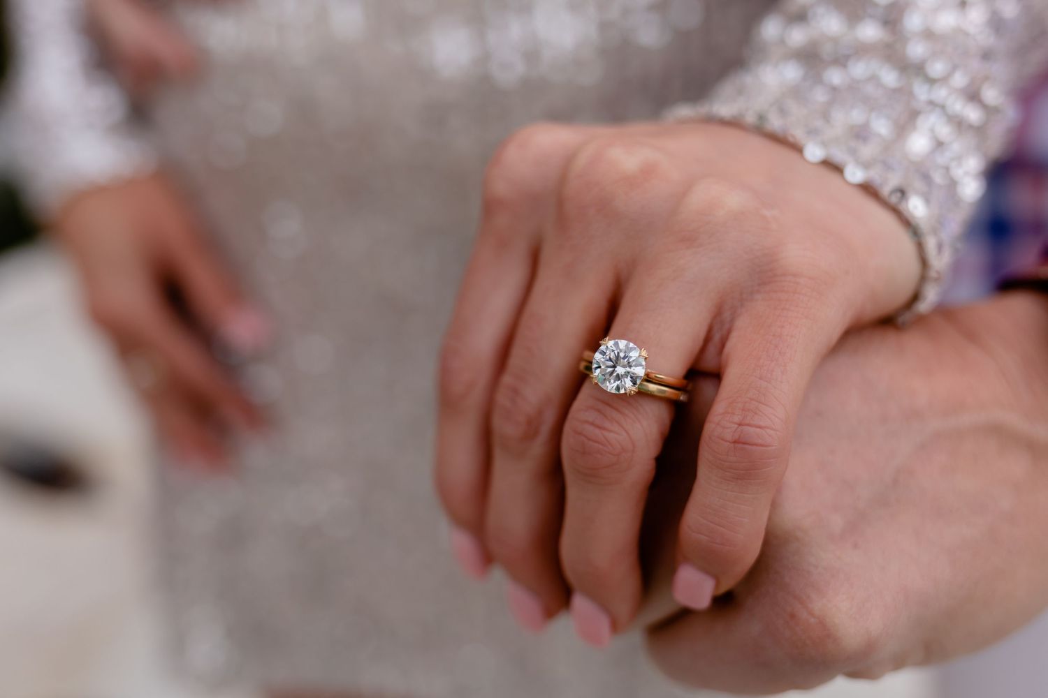 Close up shot of an engagement ring with a brilliant diamond on a hand against a sparkly background.