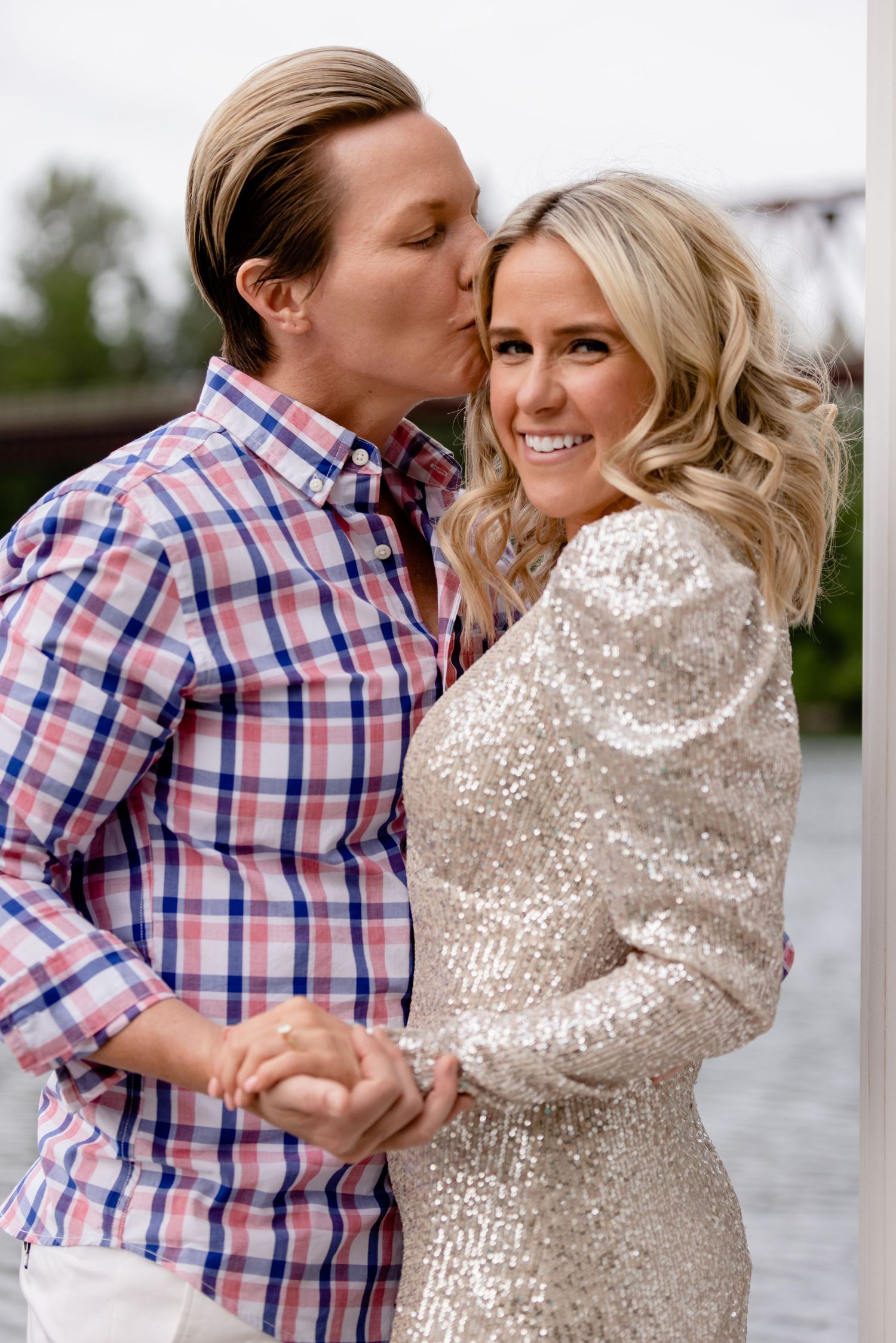 A romantic moment shared between a couple wearing a sequin dress and plaid shirt by the water.