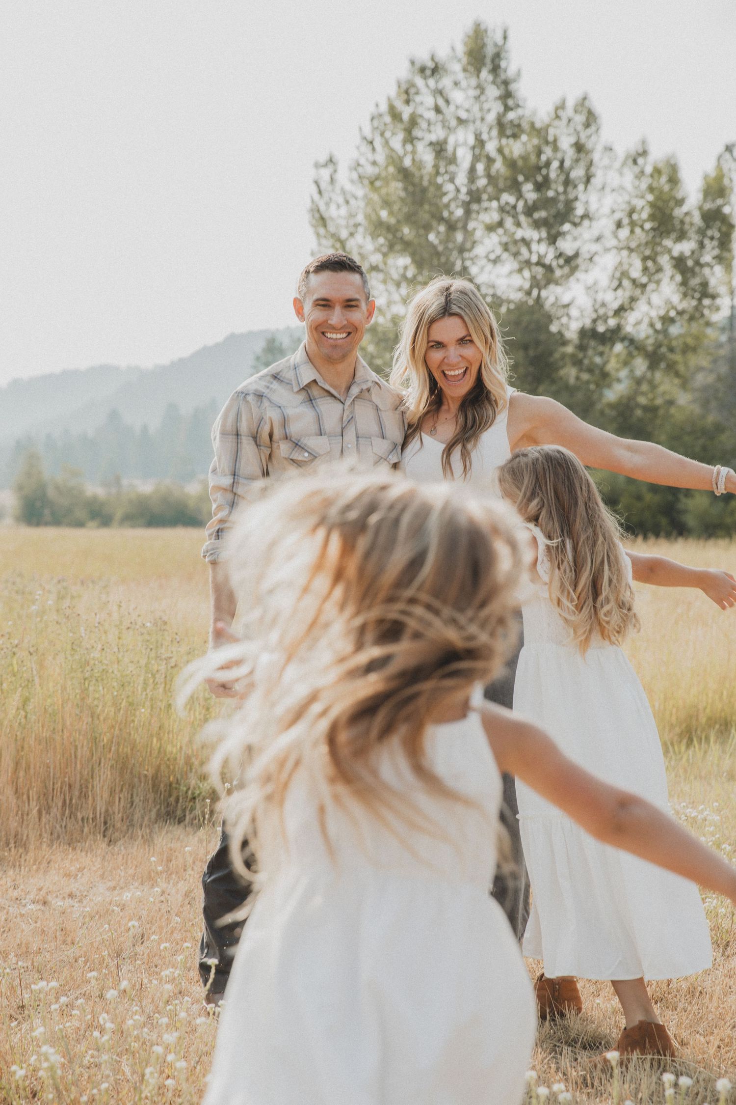 A joyful family moment captured in a sun-drenched field with mountains in the background.