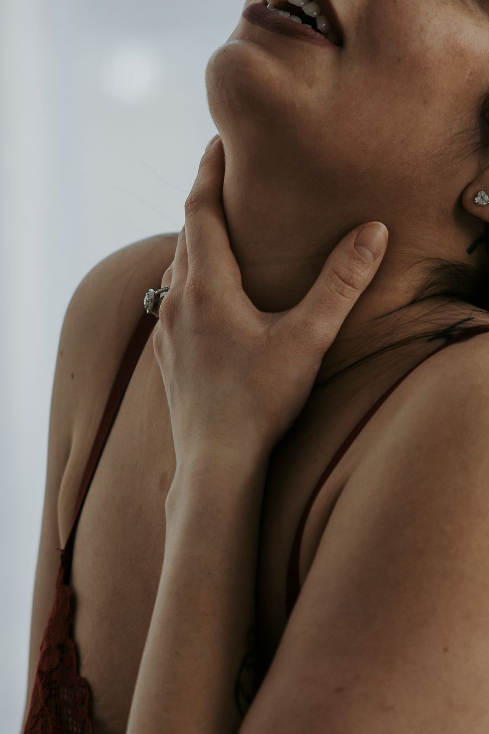 Artistic closeup of a hand delicately placed on neck wearing a ring with moody lighting and brown tones.