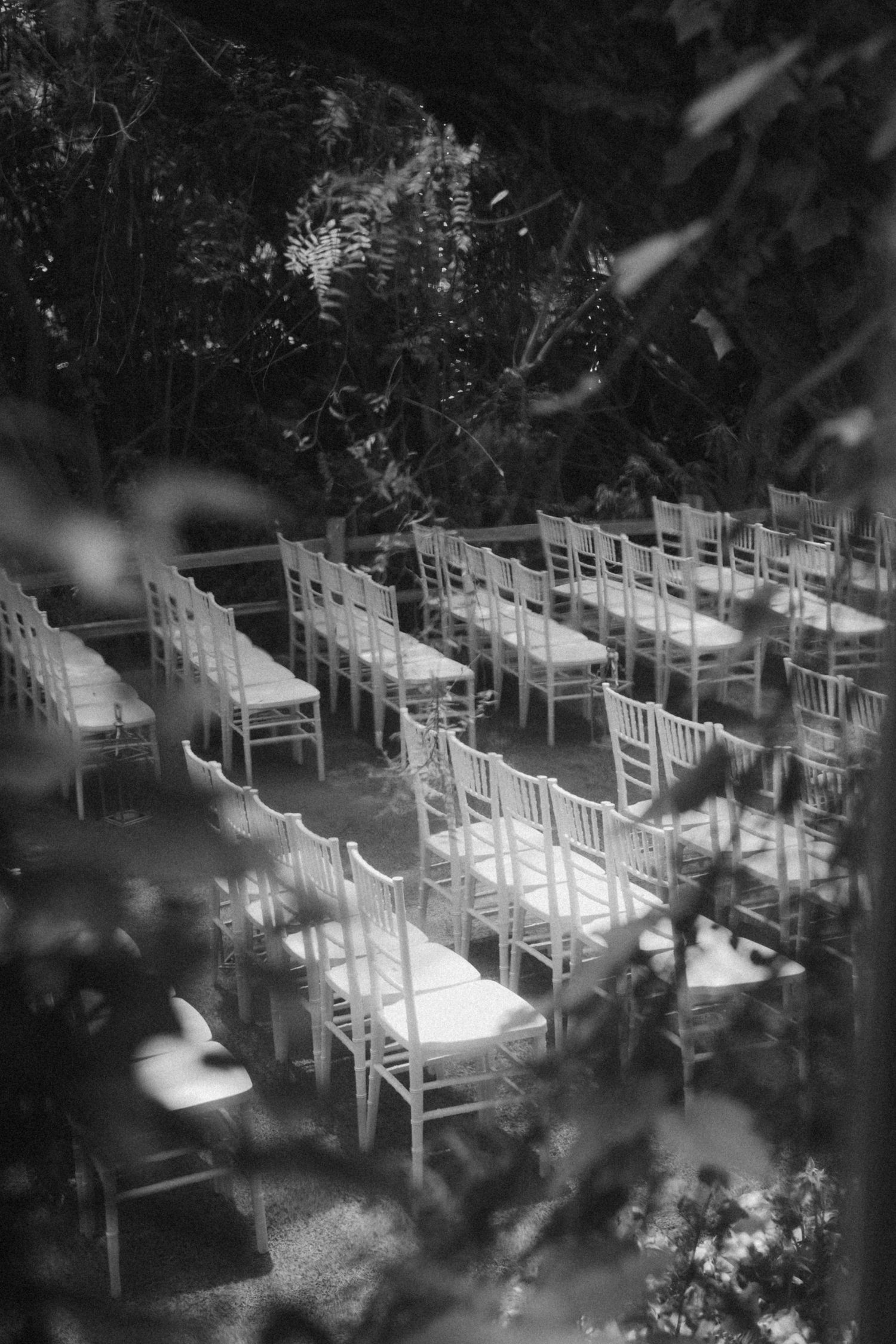 Black and white photo of white wooden chairs arranged in rows for an outdoor ceremony or event.