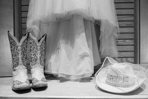 Black and white photo of cowboy boots, a bride hat, and wedding dress hem for a country western wedding.