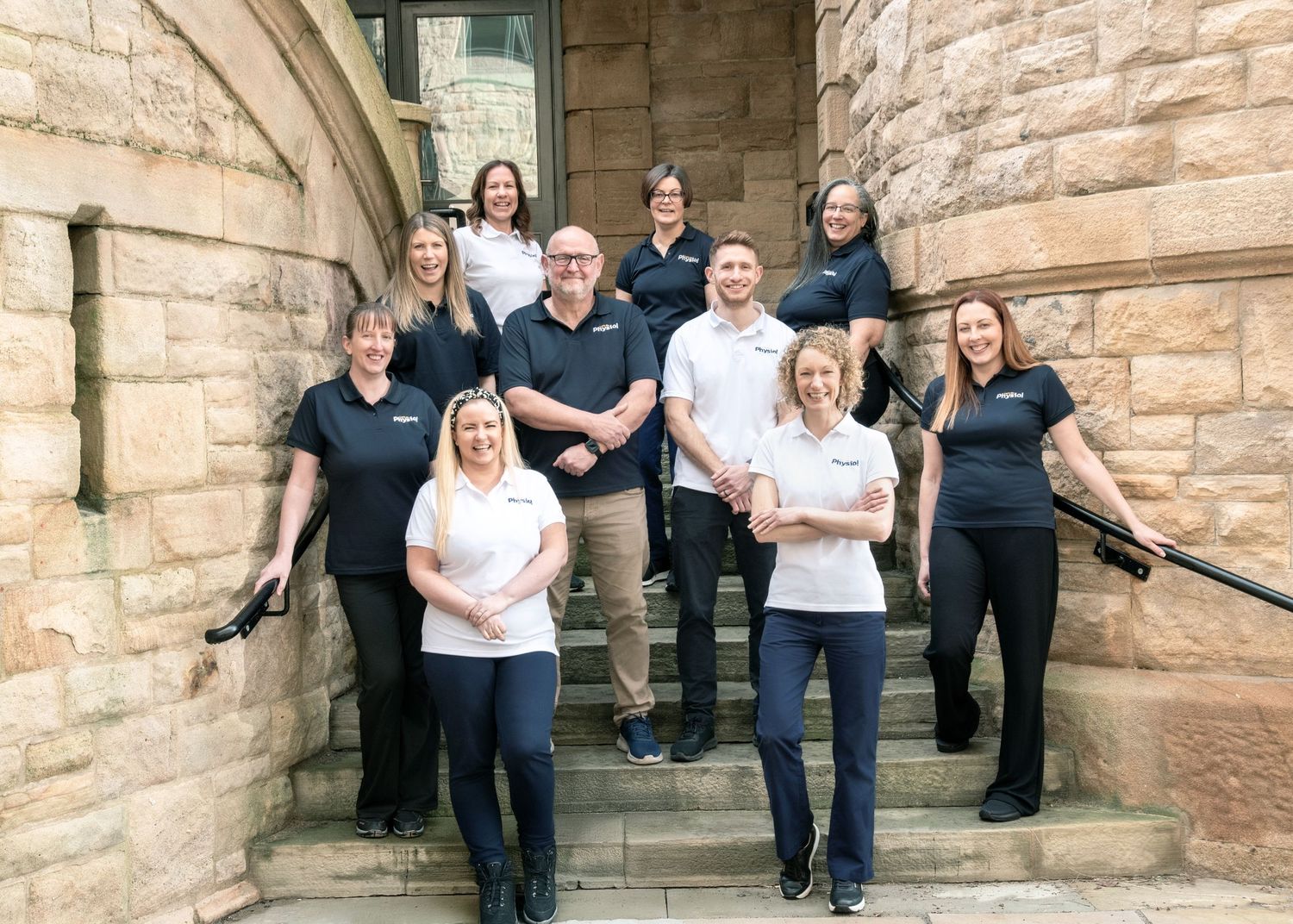 Professional group photo of team members standing on stone church steps in coordinated black and white attire.