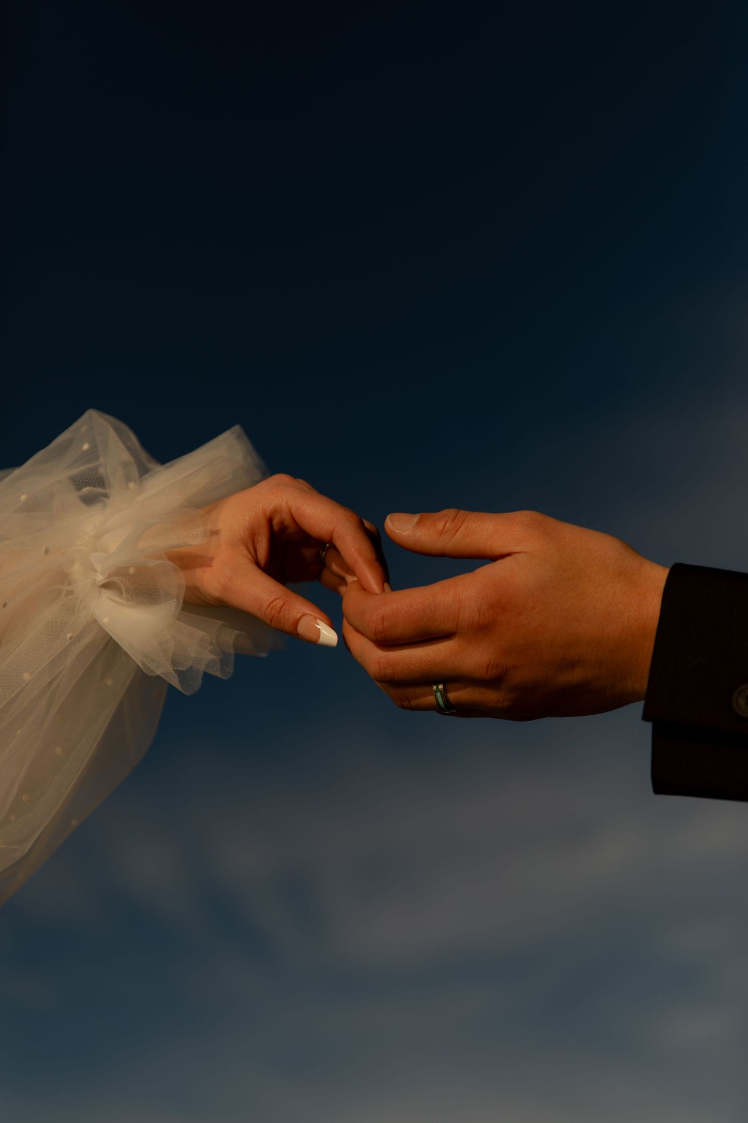 Close-up of hands exchanging rings during a wedding ceremony against blue sky.