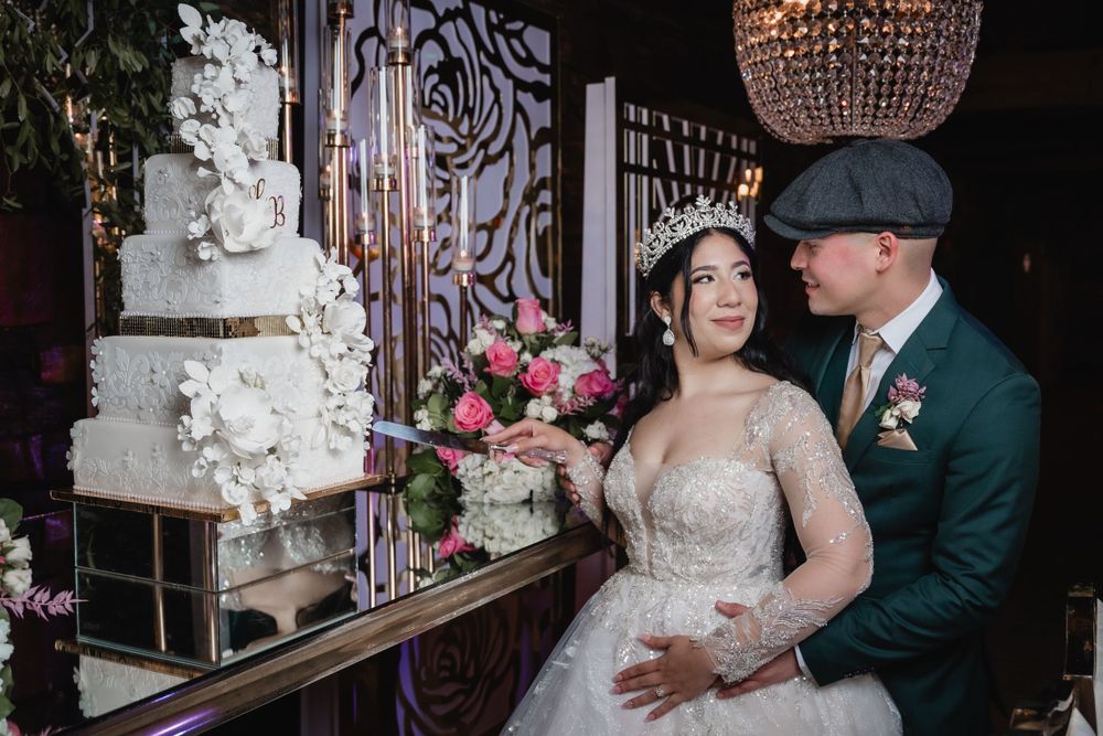 A luxurious wedding reception scene with an ornate white cake, crystal chandelier, and floral arrangements in pink and white.