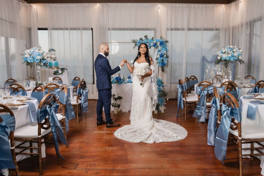 An elegant wedding ceremony setup with blue floral decor, featuring a couple at an altar and guests seated at tables.