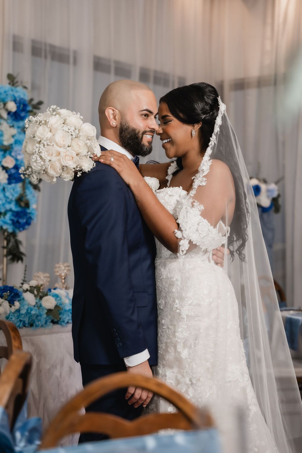 An intimate wedding portrait moment in front of a floral backdrop with blue accents.