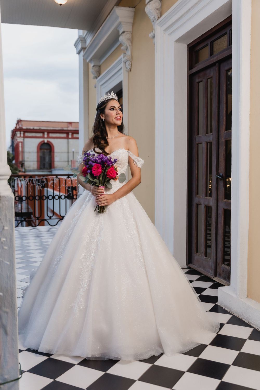 An elegant bridal portrait featuring a white ballgown and vibrant pink bouquet on a classic checkered terrace.