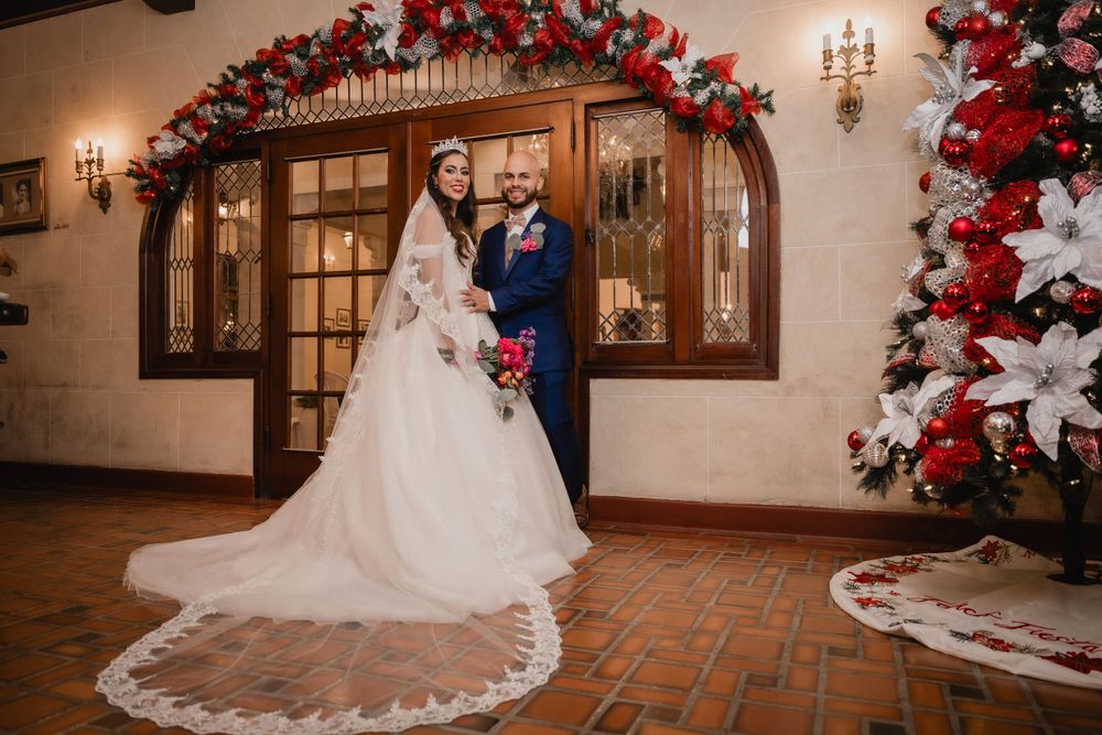 Wedding couple poses under elegant arch decorated with red and white flowers in a rustic venue interior.