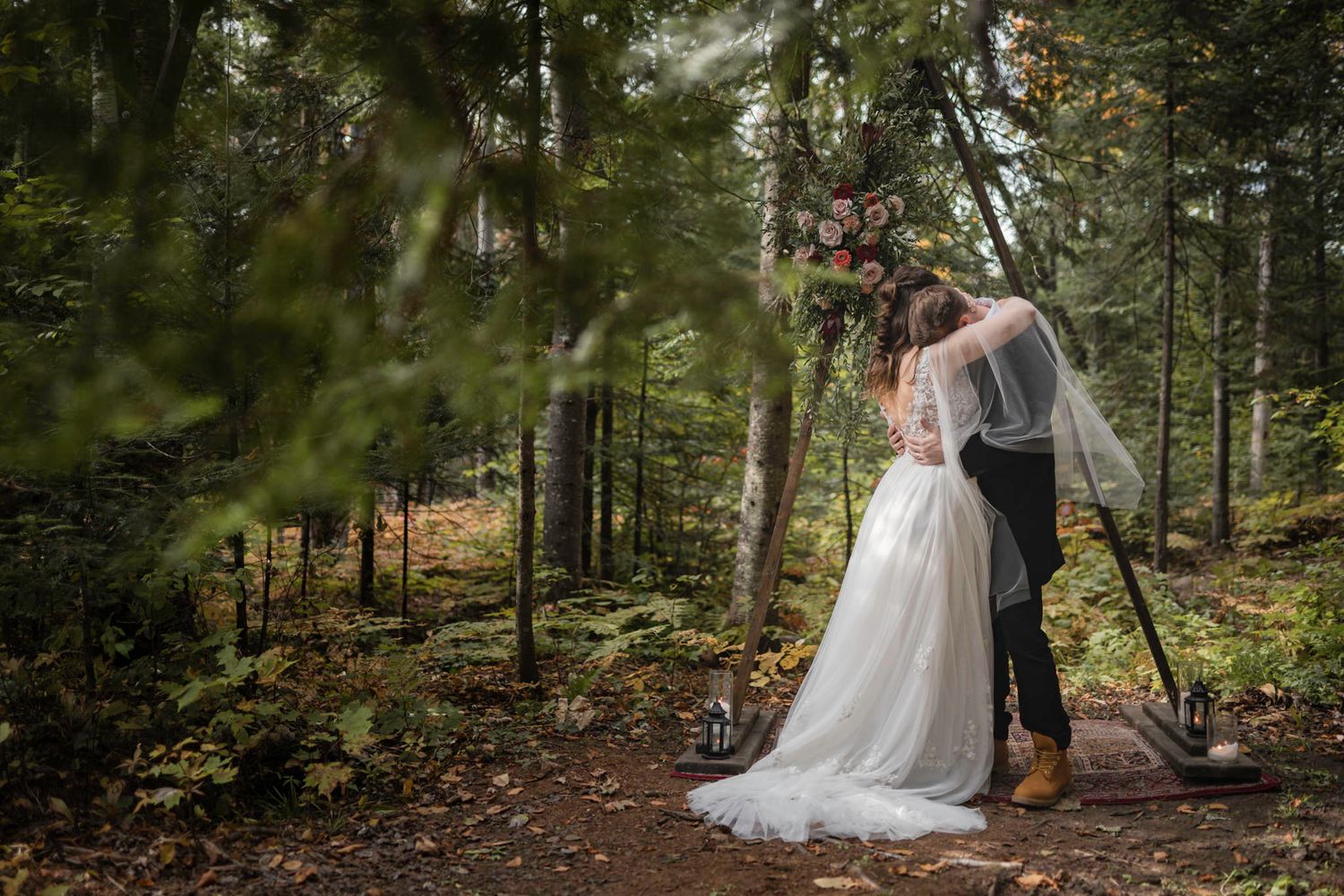 Eloping couple share an intimate hug at the archway of their ceremony in the forest in Mont Tremblant, Quebec, Canada.