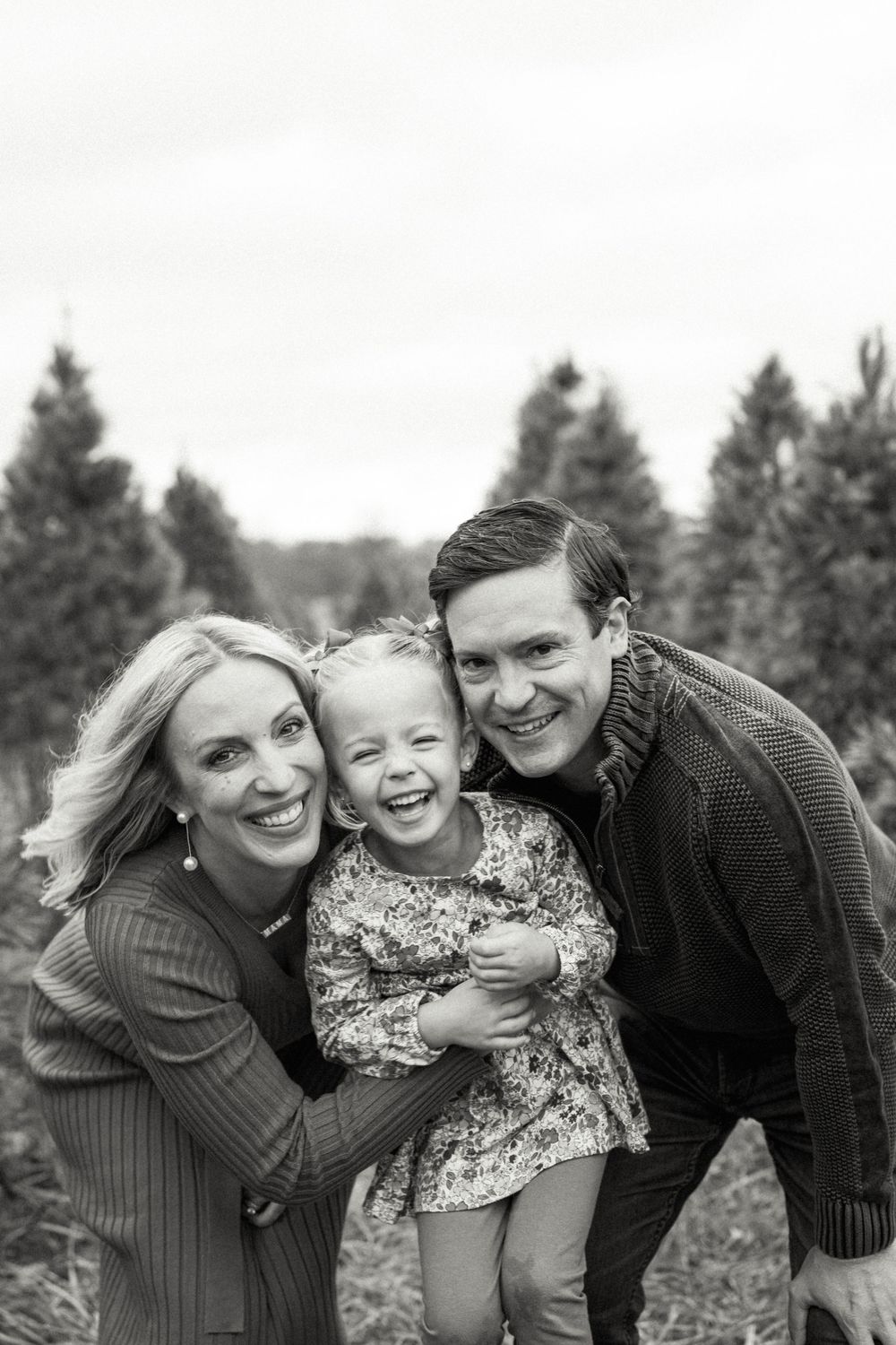 Black and white portrait of family laughing together at Christmas tree farm.