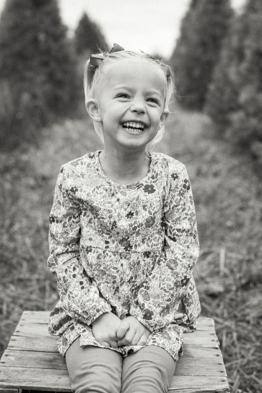 Black and white portrait of child laughing while sitting on wooden crate.