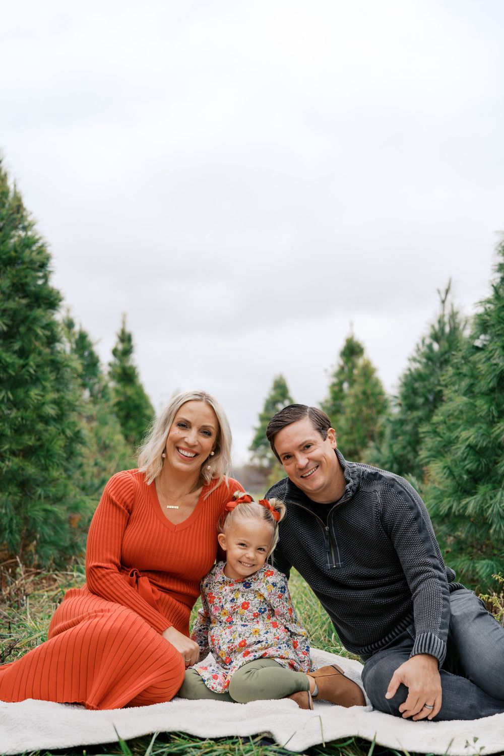 Family lying on white blanket during outdoor photo session at Christmas tree farm.